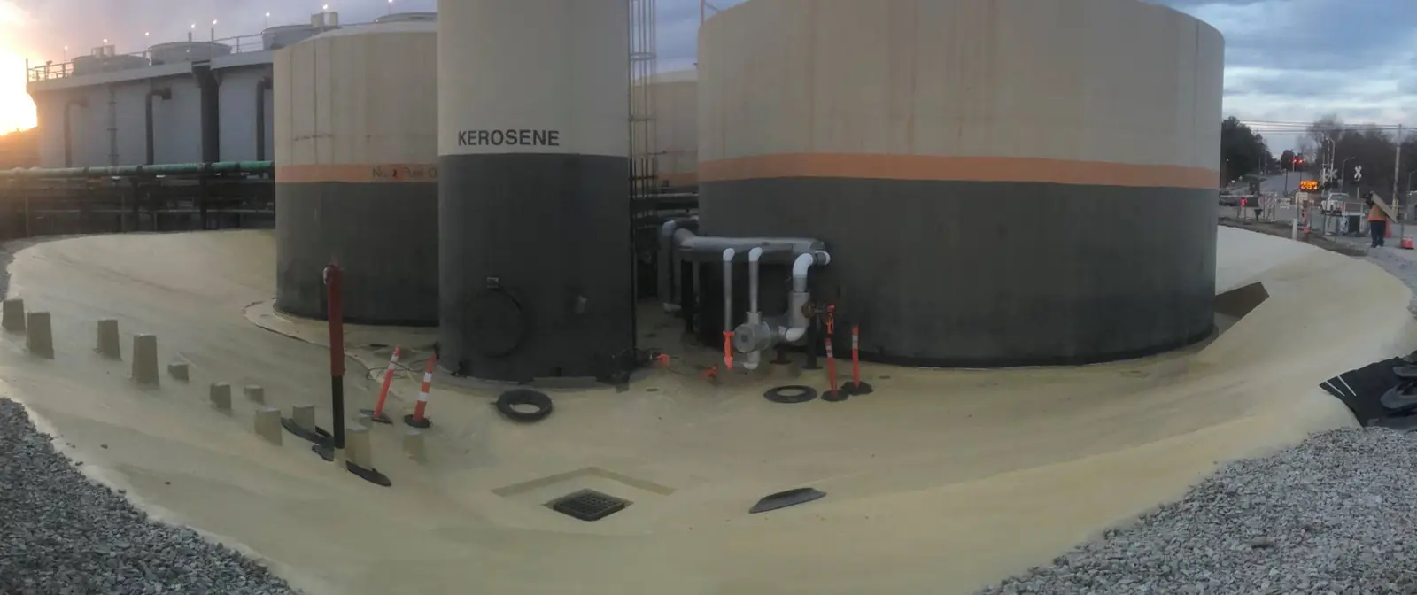 Row of large storage tanks inside a lined containment area at dusk