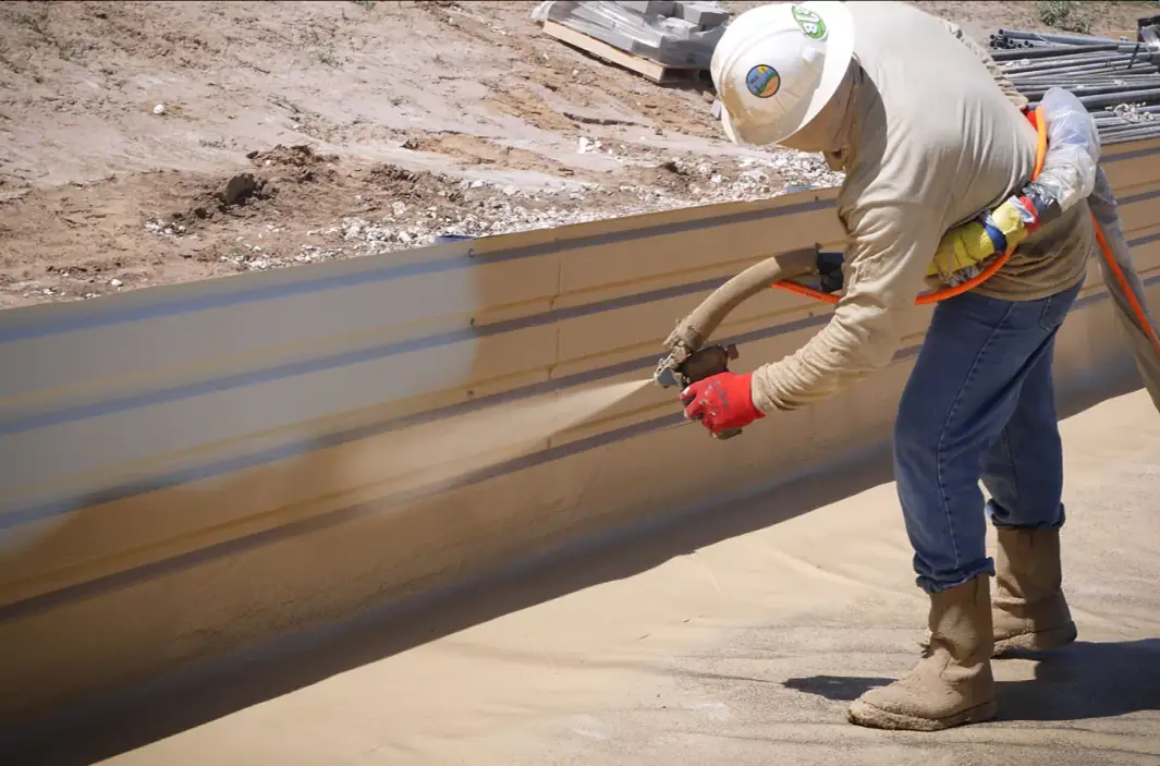Applicator in protective gear spraying a lining onto the wall of a containment berm