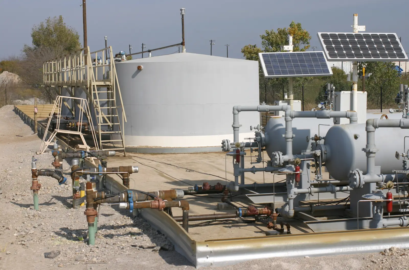Storage tank, pumps and pipework on a coated containment pad with solar panels behind