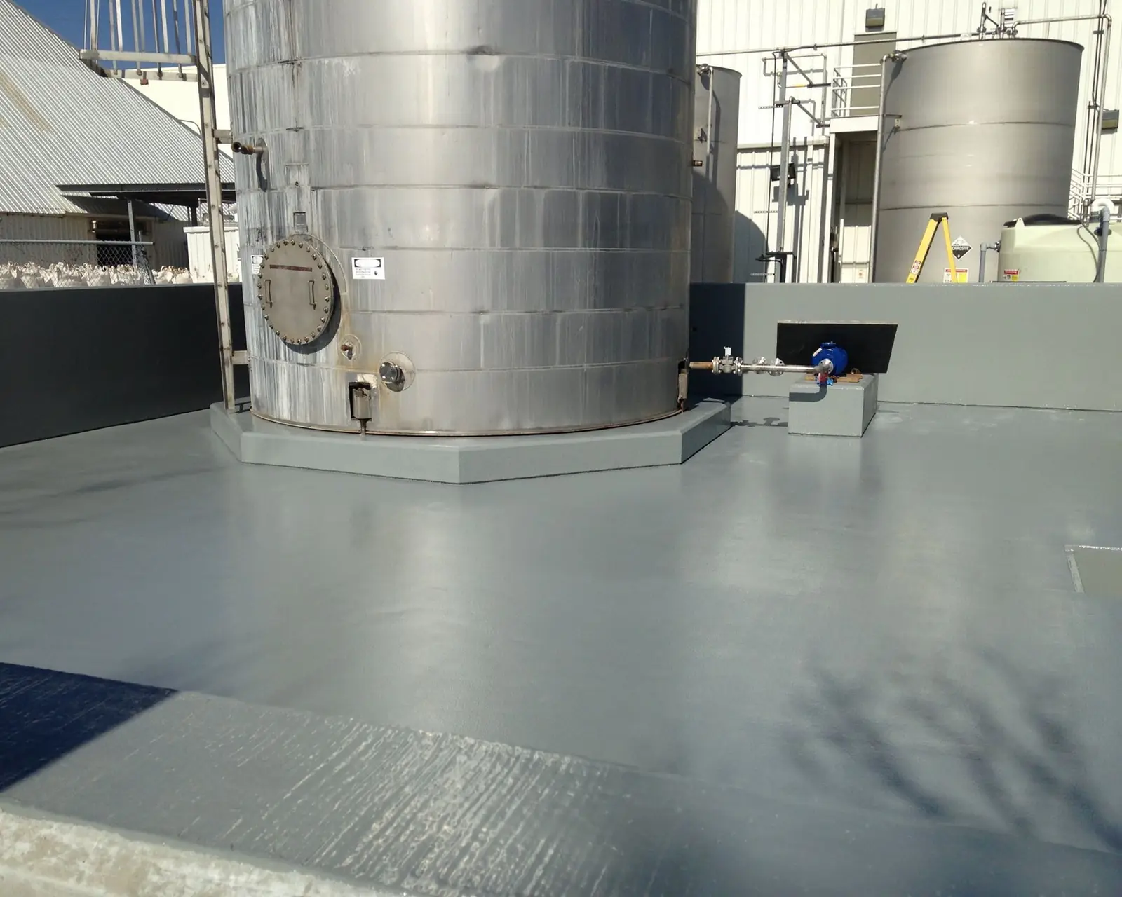 Gray coated containment floor around the base of a tall steel storage tank